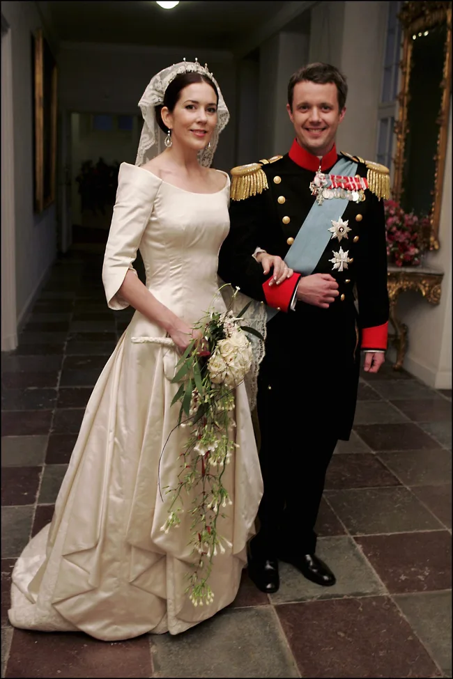 Bride in a wedding gown and groom in a military uniform pose together in an elegant hallway.