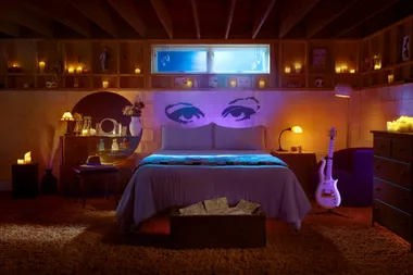 Cozy bedroom with purple lighting, large eye mural above bed, candles, guitar, and soft ambient glow.