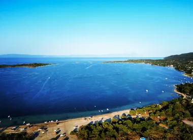 Aerial view of a wide expanse of blue sea surrounded by green coastline with small boats along the shore under a clear sky.