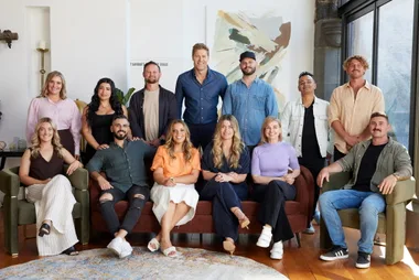 Group photo of thirteen people smiling indoors, some seated and others standing, with abstract art in the background.