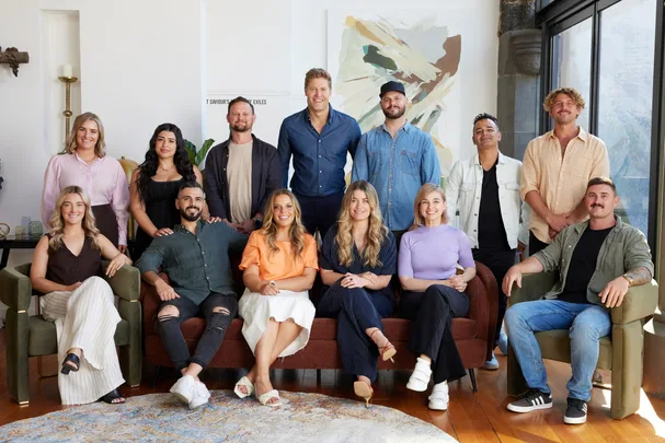 Group photo of thirteen people smiling indoors, some seated and others standing, with abstract art in the background.