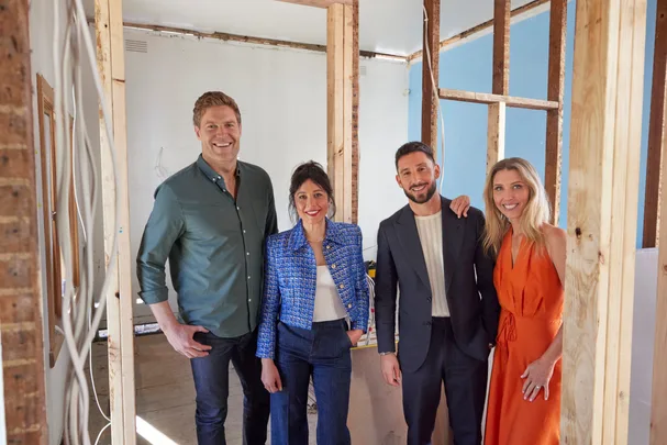 Four people smiling in a partially constructed room with exposed wooden beams.