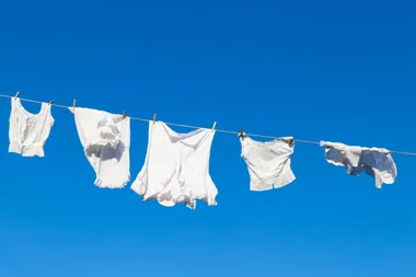 Clean white laundry hanging to dry on a rope against the blue sky during a beautiful sunny day