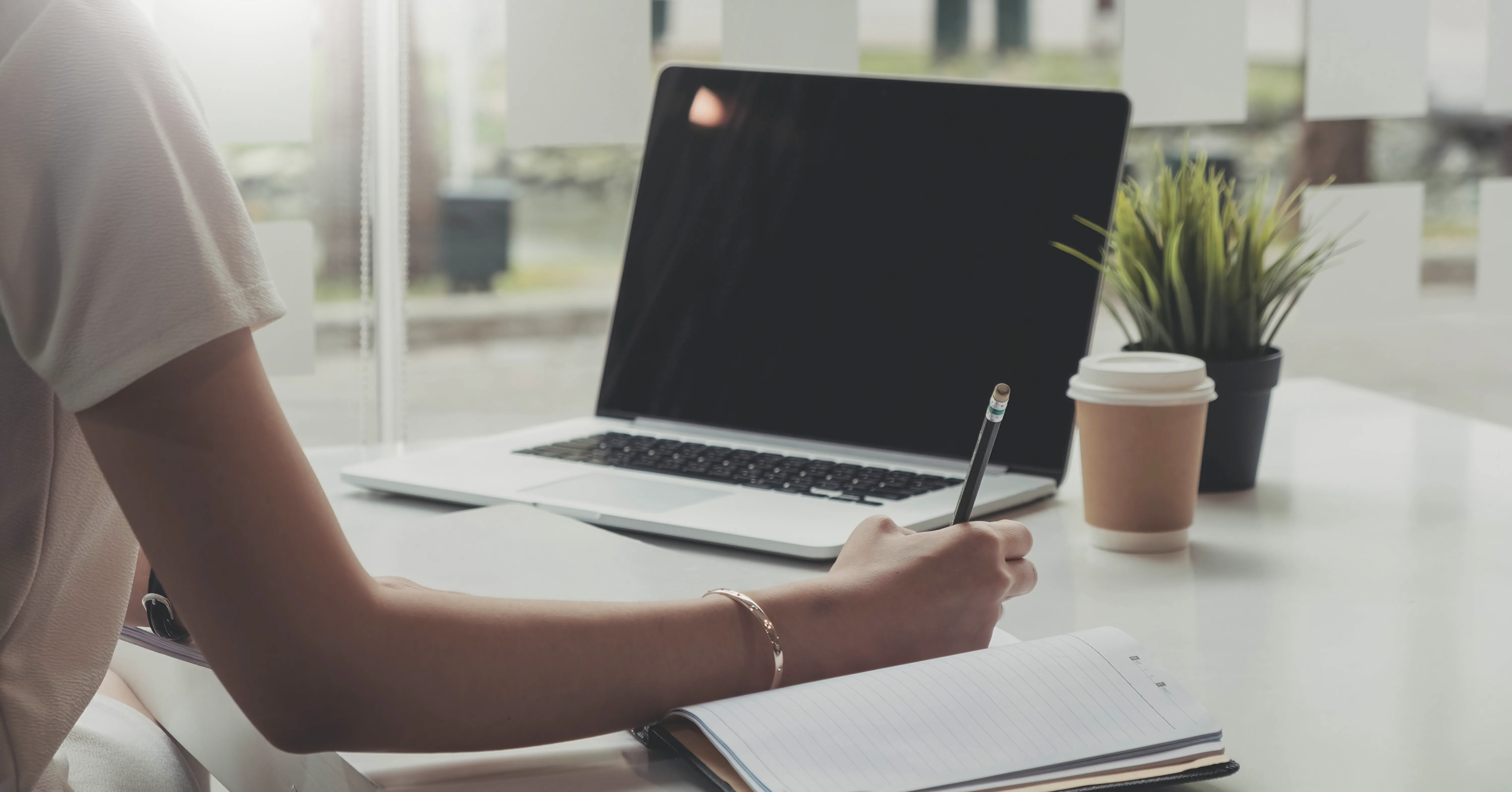 A woman writing notes while looking at a laptop. 