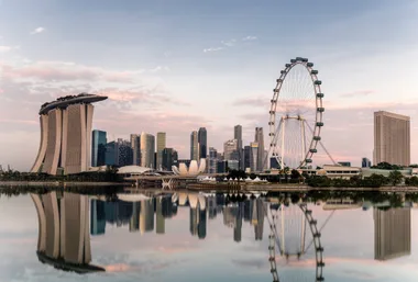 Singapore skyline with Marina Bay Sands, Singapore Flyer, and cityscape reflecting in water at sunset.