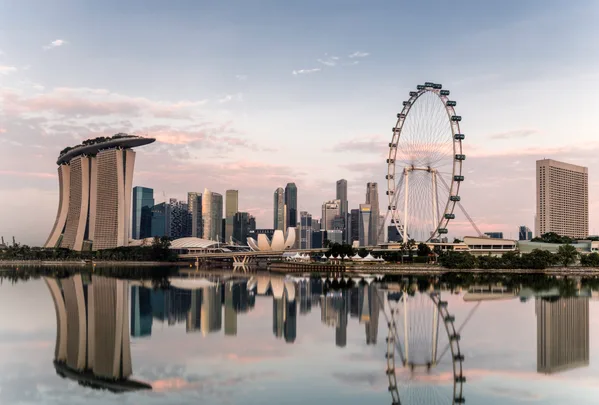 Singapore skyline with Marina Bay Sands, Singapore Flyer, and cityscape reflecting in water at sunset.