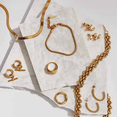 Gold jewelry set including a necklace, bracelet, earrings, and rings displayed on marble slabs.