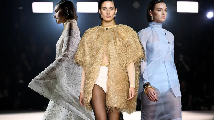 Models showcasing diverse outfits at a fashion show runway, including a gold textured ensemble.