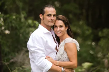 A couple smiling and embracing outdoors in a lush forest setting.