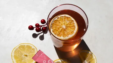 A glass of iced tea with a slice of dried orange, fresh lemon slices, and red berries on a light surface.