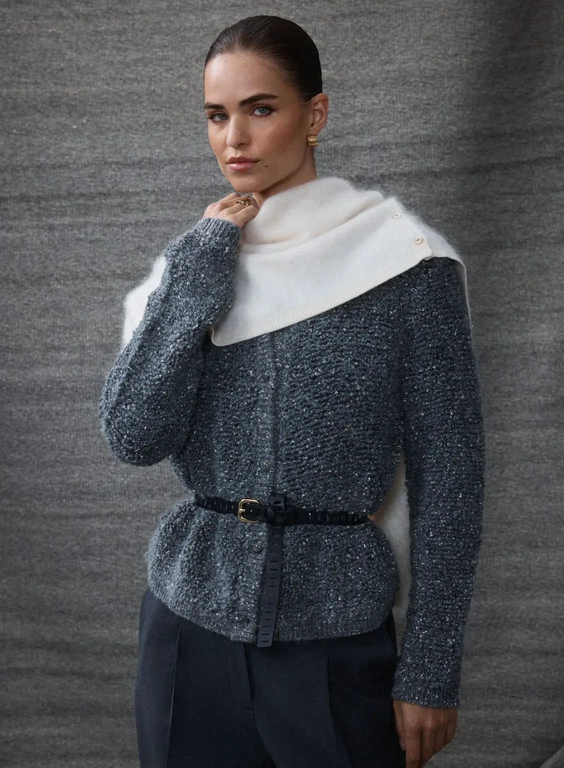 A model wearing a charcoal grey Teddy Knit Cardigan with a subtle boucle texture. The cardigan is cinched at the waist with a slim black belt and styled with a cream knit snood and dark tailored trousers. Best knitwear brands Australia article.