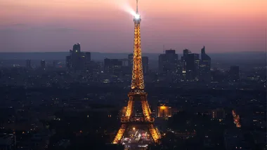 Eiffel Tower illuminated at dusk with Paris skyline in the background.