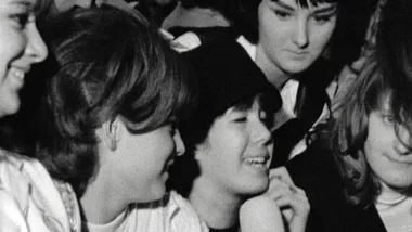 Black and white photo of five young women smiling and engaged in conversation, with 1960s hairstyles.