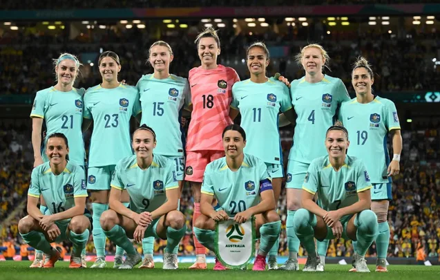 Australia women's soccer team in teal uniforms posing on field before a match.