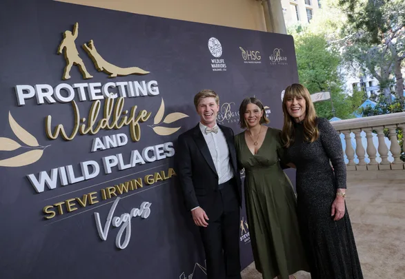 Three people smile at the Steve Irwin Gala in Vegas, standing before a "Protecting Wildlife and Wild Places" backdrop.