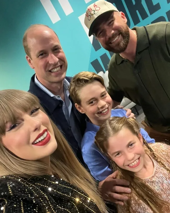 Group selfie with five smiling people indoors against a teal background.