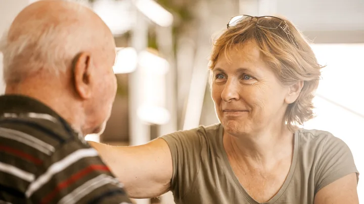 Elderly woman smiling warmly at an older man, creating a comforting and caring atmosphere.