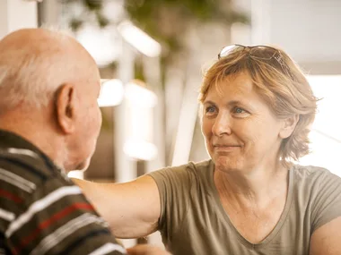 Elderly woman smiling warmly at an older man, creating a comforting and caring atmosphere.