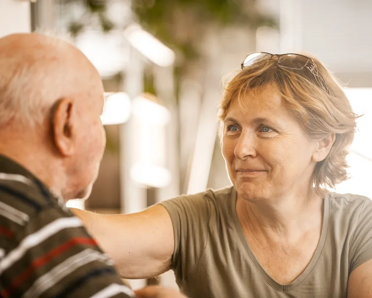 Elderly woman smiling warmly at an older man, creating a comforting and caring atmosphere.