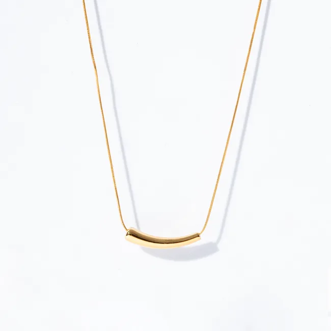 Gold curved tube pendant necklace on a fine gold chain against a white background.
