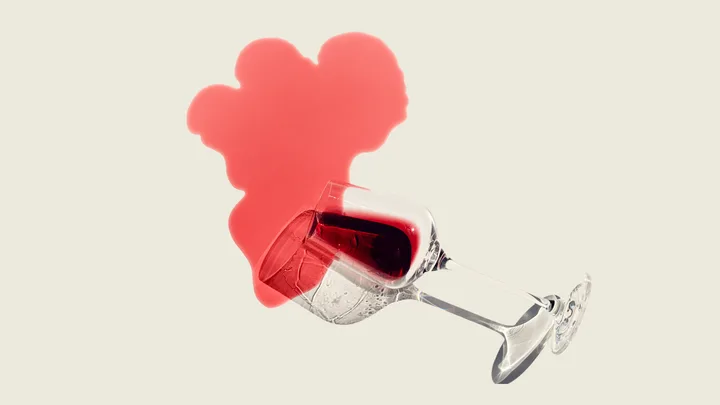 Spilled red wine glass with stain shaped like a heart on a pale background.