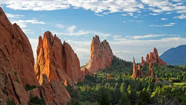 Red sandstone rock formations with greenery and a bright blue sky at Garden of the Gods, Colorado Springs.