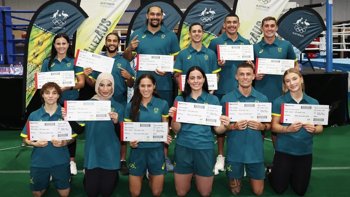 Australian athletes pose with boarding passes for the Paris 2024 Olympics, standing in front of branded banners.
