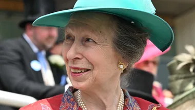 Elderly woman in turquoise hat and pearl earrings, smiling at an outdoor event.