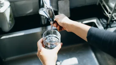 Person filling a glass with water from a kitchen sink tap.