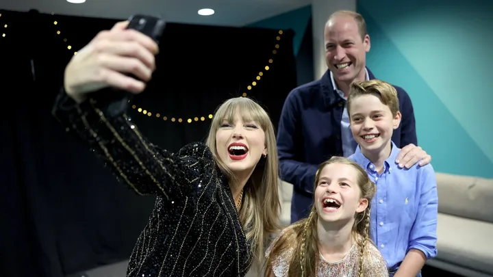 A group of people smiling and taking a selfie together in a room with festive string lights.