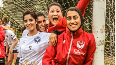 Group of women soccer players from Melbourne Victory smiling at the camera near a goalpost.
