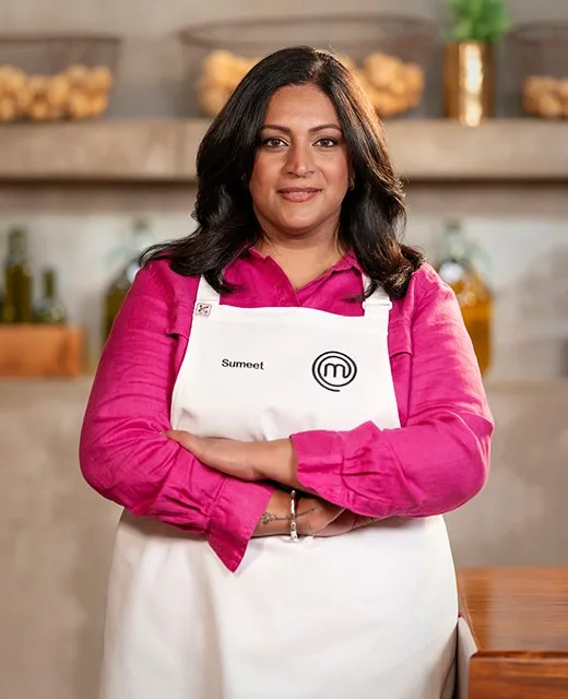 A woman in a MasterChef apron with "Sumeet" written on it, standing confidently in a kitchen setting.