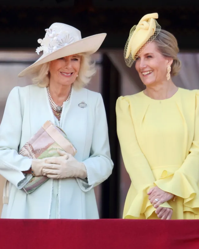Two women in elegant hats and dresses smiling at an outdoor event.