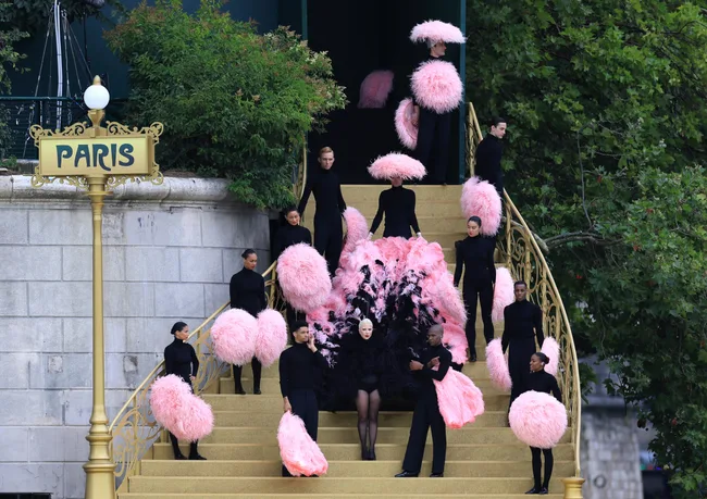 Fashion show on Paris steps; models in black with large pink feather fans.