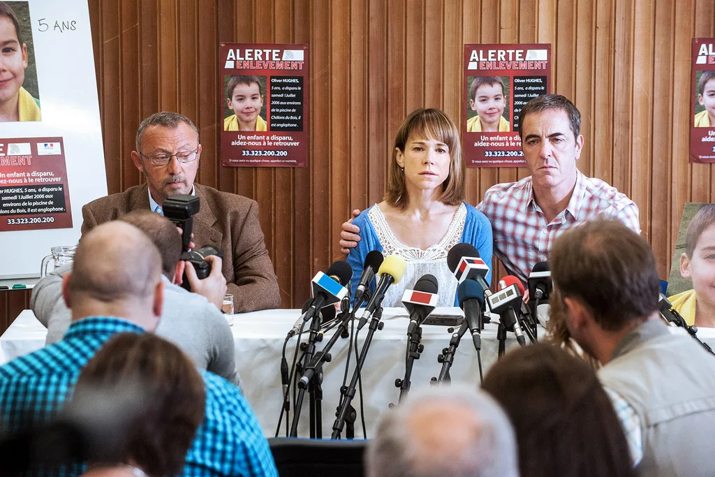 Press conference scene with three people; missing child alert posters in the background, several microphones in front.