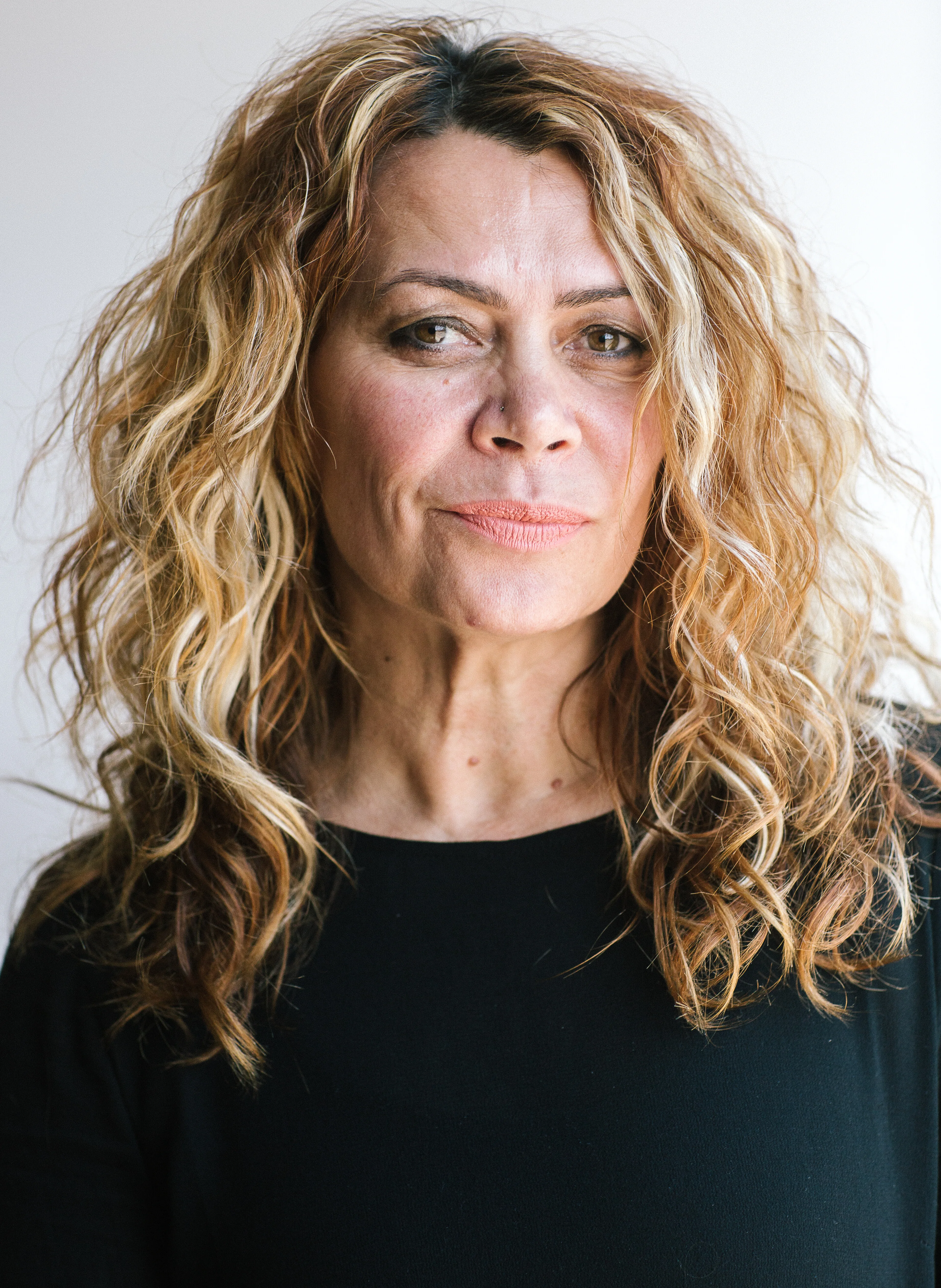 Antoinette Braybroook looks directly and seriously at the camera. She wears a black top and has long, honey-blonde, curly hair.