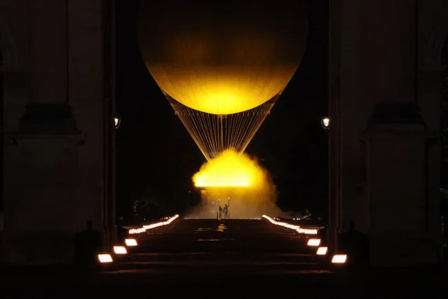 A large illuminated yellow balloon with glowing fog beneath, framed by archway in a nighttime setting.
