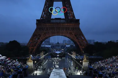 Eiffel Tower at night with Olympic rings, crowds on either side, and a lit-up pathway leading towards Vincennes.
