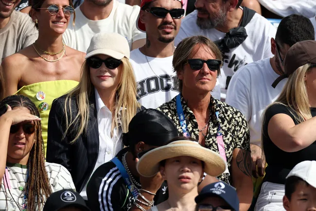 Spectators at an outdoor event, some wearing sunglasses and hats, enjoying a sunny day in a crowded audience.