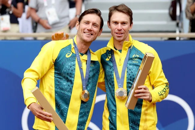 Two athletes in yellow and green outfits celebrate winning medals at a sports event, holding their gold medals and trophies.