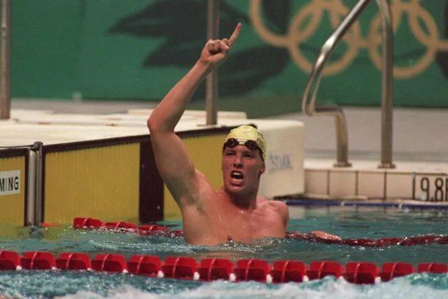 Swimmer in Olympic pool celebrates with raised index finger.