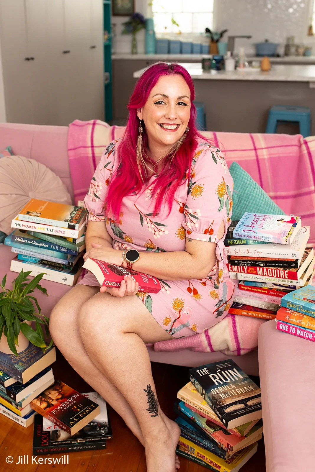 Portrait photo of rom com author Melanie Saward, a woman with pink hair wearing a pink dress.