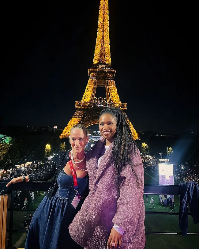 Two women smiling in front of the illuminated Eiffel Tower at night.