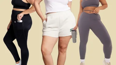 Three women wearing activewear: black leggings, white shorts, and grey leggings holding a tumbler, on a beige background.