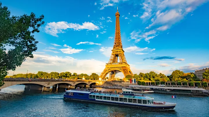 The Eiffel Tower in Paris with a boat on the Seine River, under a clear blue sky.