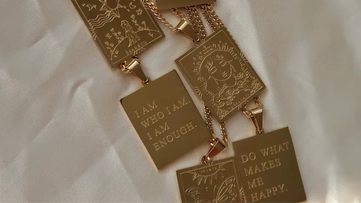 Gold engraved pendants on a chain with affirmations: "I am who I am. I am enough" and "Do what makes me happy."