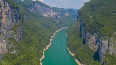 Aerial view of a river winding through lush green canyon cliffs on a sunny day.