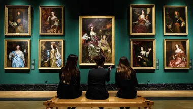 Three people sitting on a bench view historical portraits in a gallery with green walls.