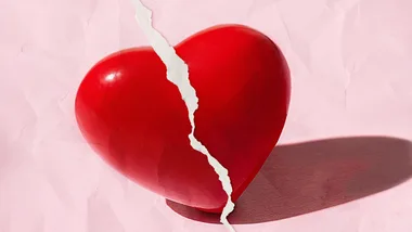 A red heart with a jagged white paper tear running vertically, set against a pink textured background.