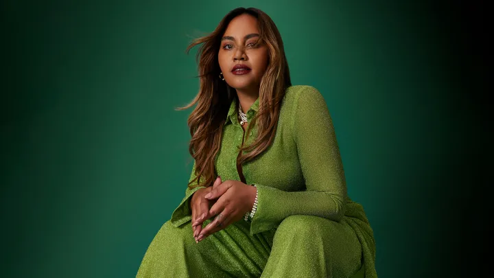 A woman in a sparkly green outfit poses confidently against a matching green background.